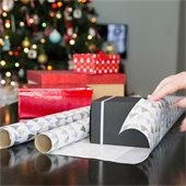 the hand of someone wrapping a gift with gifts and a tree in the background