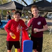 two boys standing by a giant connect four game holding soda