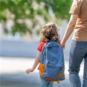 student's back as they walk holding parent's hand